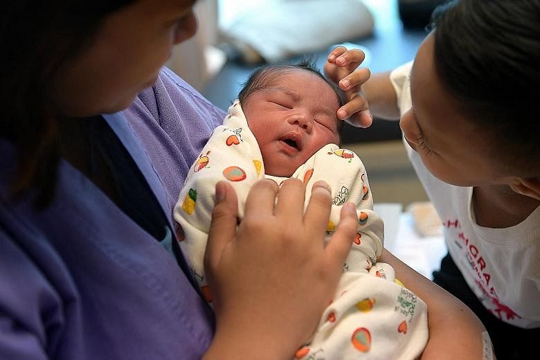 Liam Koh (left) and Abbie How are among the three babies born at the stroke of midnight on the first day of 2018. Madam Norfarizah Ambiak cradling her newborn baby, Nas Muhammad Niklas, as her oldest child, Nas Muhammad Nesta, strokes his little brot
