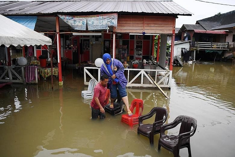 A resident of Kampung Gudang Rasau in Kuantan, Mr Mohamad Sukri, helping his wife Ita Daud get to dry land using stacked plastic chairs as a bridge after the nearby Sungai Belat overflowed its banks. More than 7,000 people have been evacuated from th
