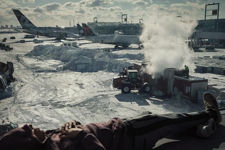 A passenger catching up on sleep as airport staff cleared snow on the tarmac at New York's John F. Kennedy Airport on Friday. Some planes spent up to four hours on the tarmac waiting for a gate. As of Saturday, more than 3,420 flights within, into or