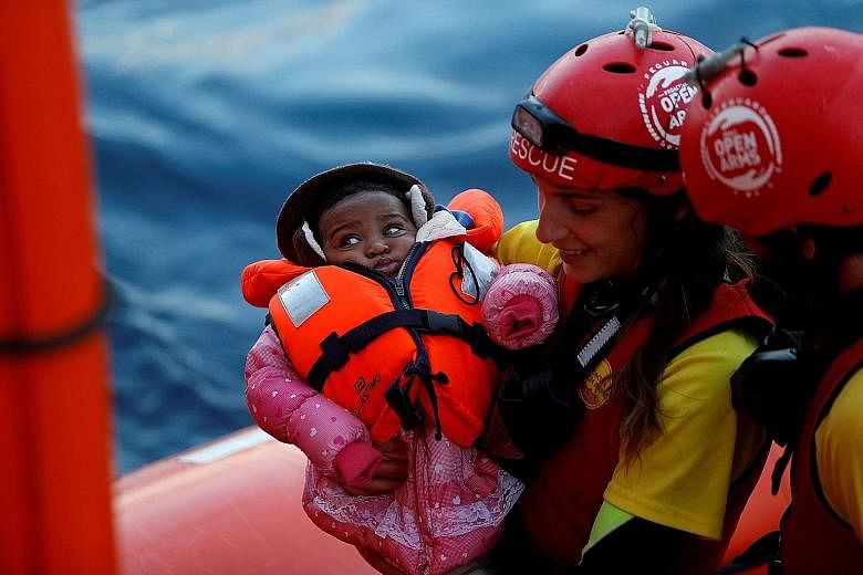 Above: A refugee from Lebanon in the small German village of Clausnitz, in Saxony, in 2016. Left: A rescue team with a migrant child during a mid-sea transfer of refugees in the central Mediterranean off the coast of Libya last month.