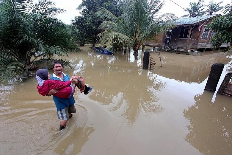 Mr Azhar Osman, 56, carrying his 75-year-old mother Rabayah Abdul Hamid to safety after floodwaters inundated his house compound at Kampung Gudang Rasau yesterday. The flood situation in the state of Pahang eased slightly with the number of evacuees 