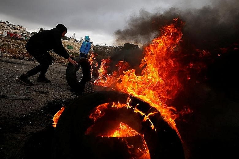 A Palestinian moving a burning tyre during clashes with Israeli troops at a protest against the visit of US Vice-President Mike Pence to Jerusalem yesterday. The US' recognition of Jerusalem as Israel's capital has broken with decades of internationa