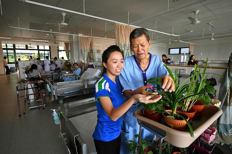 Occupational therapist Giang Thuy Anh, 28, with a patient during mobile horticulture therapy in Yishun Community Hospital's acute geriatric ward. The programme, which takes plants to the patients' bedside, was started last year to improve their level