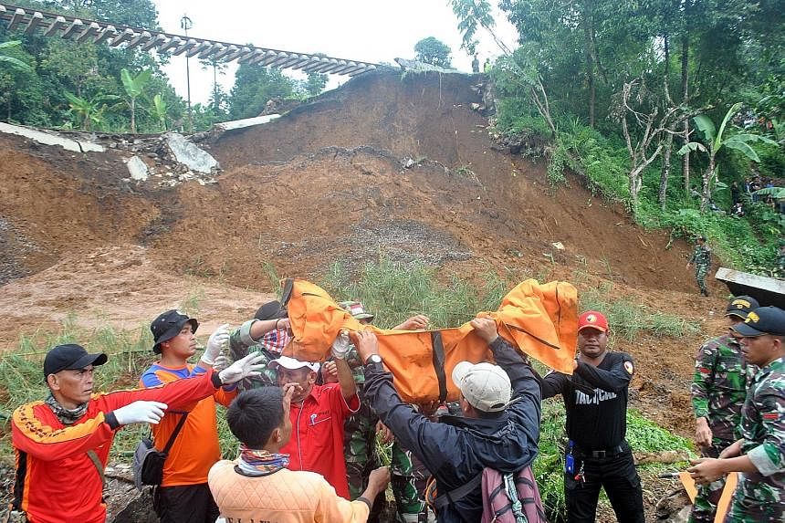 Residents of a Jakarta neighbourhood (left) carrying their belongings as they wade through flood waters yesterday. Rescue workers (above) recovering the body of a landslide victim in Bogor regency, West Java.