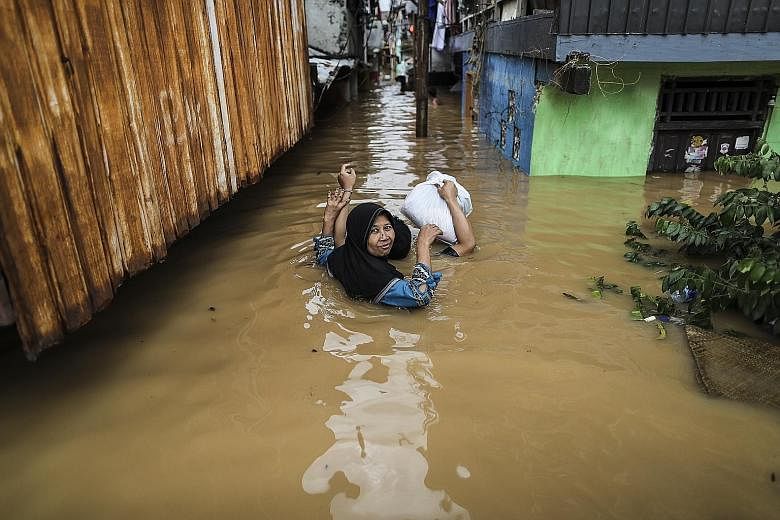 Residents of a Jakarta neighbourhood (left) carrying their belongings as they wade through flood waters yesterday. Rescue workers (above) recovering the body of a landslide victim in Bogor regency, West Java.