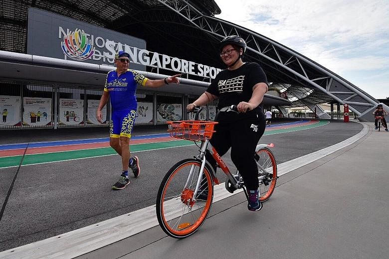 An OCBC Cycle participant cycling a Mobike while wearing a helmet under the watchful eye of OCBC Cycle's Project Training Wheels coach Michael Lyons at the Sports Hub.