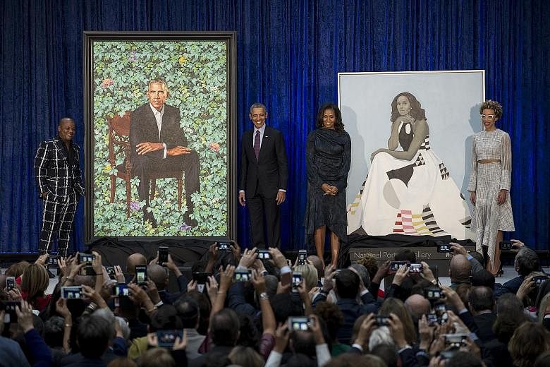 Former United States president Barack Obama and his wife Michelle (both centre) with their official portraits by artists Kehinde Wiley (left) and Amy Sherald (right).