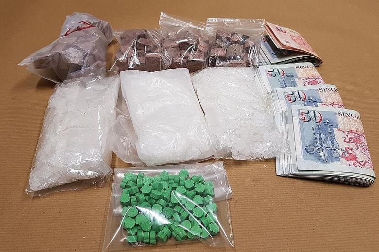 Heroin, Ice, Ecstasy tablets as well as cash (top) were recovered during a Central Narcotics Bureau operation on Monday. CNB officers also found four parangs and a baton (above).
