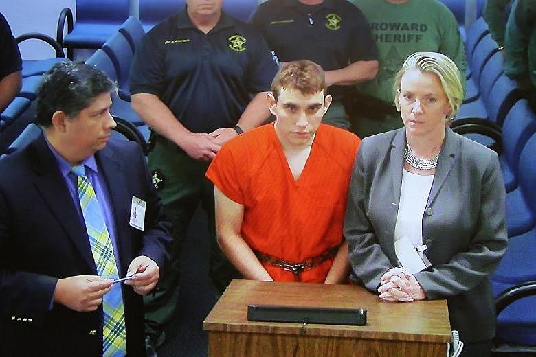 Above: Mourners grieving as they wait for a candlelight vigil to begin in Parkland on Thursday. Below: Suspect Nikolas Cruz (centre) at a Broward County court, where he was charged with 17 counts of premeditated murder. Initial reports point to a tro