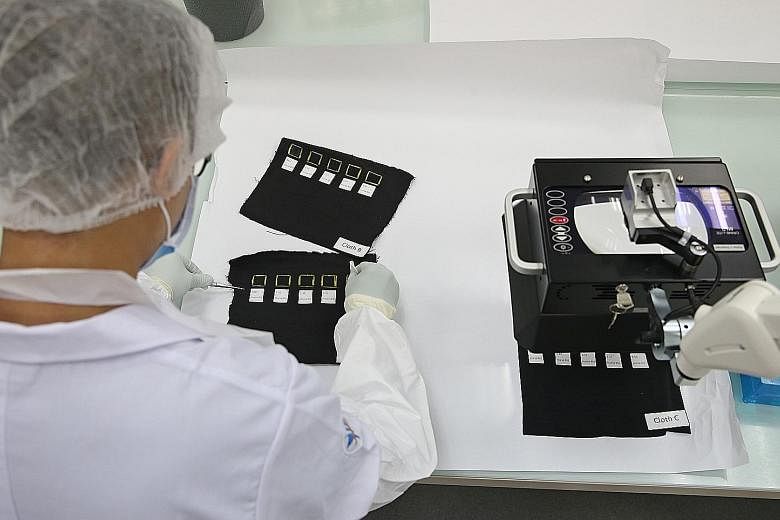 A lab officer examines a shirt as part of the training to look for traces of DNA left behind at crime scenes. A laboratory officer (left) examines different dilutions of blood on pieces of black cloth. While blood on dark cloth may not be visible to 