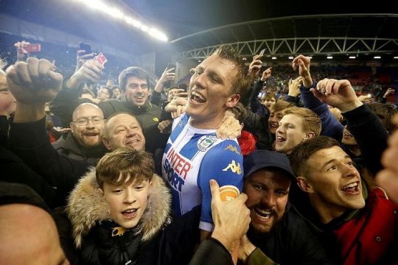 Wigan's Dan Burn soaking up the post-match jubilation with fans who thronged the pitch after the final whistle. The League One side may face punishment after some fans got into a scuffle with City striker Sergio Aguero amid the celebrations.