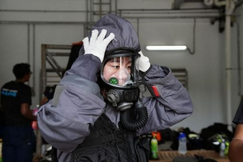 Straits Times reporter Cheryl Tee puts on a chemical agent suit (above) and a light decontamination suit during her visit to the Home Team Tactical Centre earlier this month. During training and operations, marine firefighters wear equipment weighing
