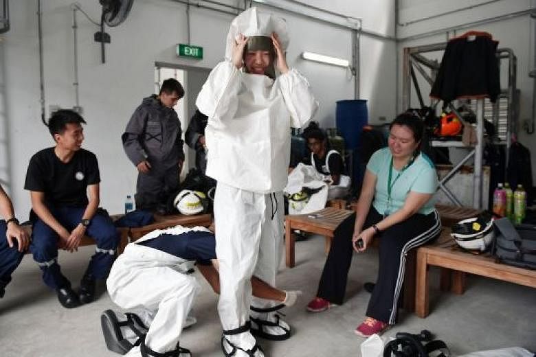 Straits Times reporter Cheryl Tee puts on a chemical agent suit and a light decontamination suit (above) during her visit to the Home Team Tactical Centre earlier this month. During training and operations, marine firefighters wear equipment weighing