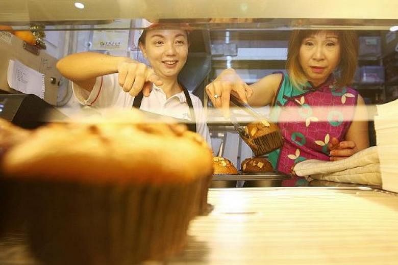 Senior Minister of State Amy Khor (right) helping Muffin Haus stallholder Tan Pey See, a former chemical engineer, display freshly baked muffins at her stall in ABC Brickworks Food Centre. 