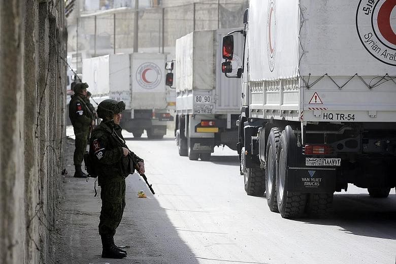 Russian soldiers standing guard as Syrian Arab Red Crescent trucks carrying aid drove by the checkpoint on the outskirts of Damascus neighbouring the eastern Ghouta region, as they headed towards the rebel-held enclave yesterday.
