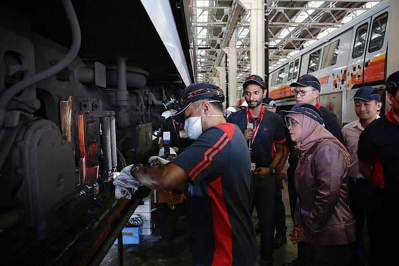 President Halimah Yacob observing maintenance work being done on the undercarriage of a train during her visit to SMRT's Bishan Depot yesterday.