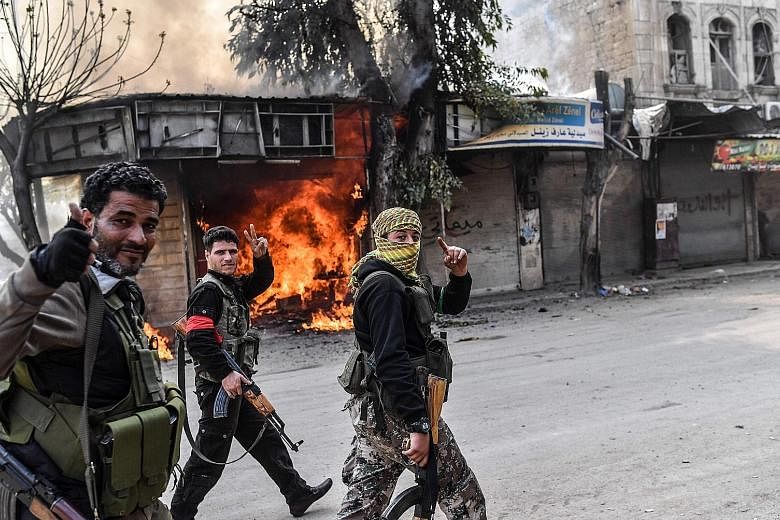 Turkish-backed Syrian rebels walking past a burning shop in the city of Afrin in northern Syria yesterday.