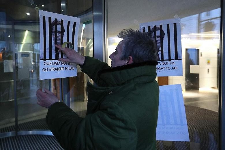 A man putting up posters depicting now suspended Cambridge Analytica CEO Alexander Nix behind bars, at the entrance of the company's offices in central London on Tuesday.