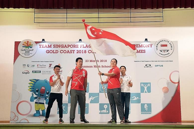 Former swimmer Mark Chay, chef de mission for the Commonwealth Games, handing the Singapore flag to shooter Teo Shun Xie at a ceremony at Dunman High School yesterday. Observing are Parliamentary Secretary for Culture, Community and Youth Baey Yam Keng (l