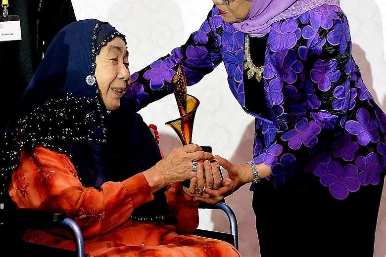 Puan Noor Aishah, 84, the wife of Singapore's first president Yusof Ishak, receiving a trophy from President Halimah Yacob. She was commended for "breathing new life" into the Istana and for her quiet determination, humility and charm.