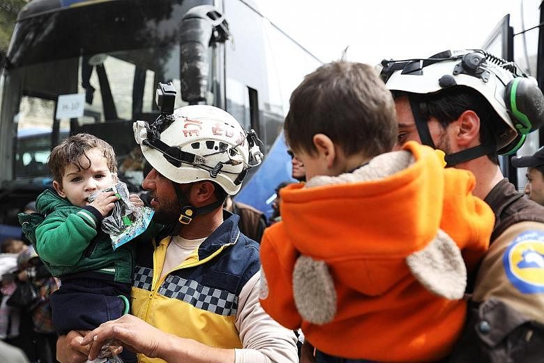 Members of the Syrian Civil Defence (known as the White Helmets) holding children as Syrian civilians and rebel fighters arrived in the village of Qalat al-Madiq yesterday, after being evacuated from Harasta in eastern Ghouta.
