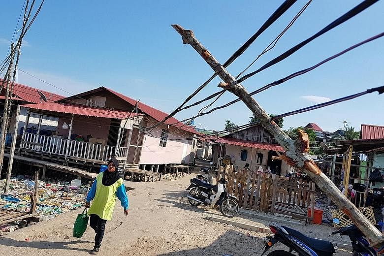 The village is poverty-striken and neglected. Electricity is wired to homes through overloaded power strips and tangled extension cords, and heaps of empty water bottles and food waste clog the coastline. Blue BN flags and red PPBM flags at the entra