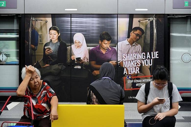 Commuters in front of an advertisement discouraging the dissemination of fake news, at a train station in Kuala Lumpur. The proposed law penalises those who maliciously create or spread such content.