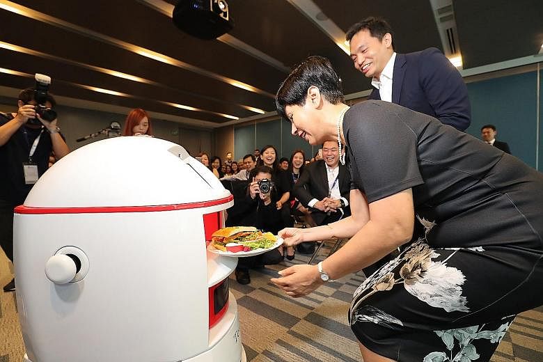 Senior Minister of State for Law and Finance Indranee Rajah getting a roast chicken sandwich, which she had ordered remotely using the mobile app, from Max the robot.