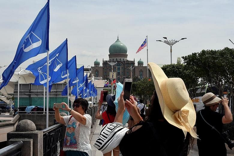 Barisan Nasional flags flying in Putrajaya as visitors capture the sights yesterday. Malaysia's ruling coalition and the opposition have unveiled help measures targeting young voters in the run-up to the May 9 elections.