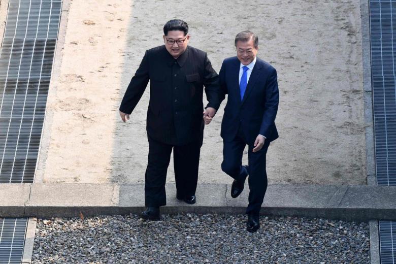 North Korea's leader Kim Jong Un (left) walks with South Korea's President Moon Jae In over the Military Demarcation Line that divides their countries as they meet at Panmunjom, on April 27, 2018.