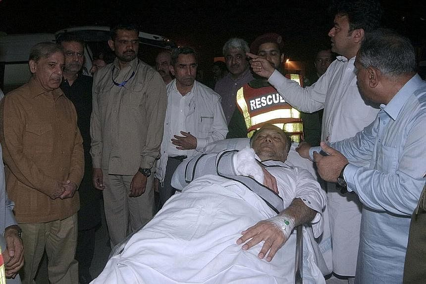 Security officials standing guard outside the hospital where Pakistani Interior Minister Ahsan Iqbal (below, on stretcher) was taken to after he was shot. A man identified by police only as "Abid" and said to be in his early 20s was wrestled to the g