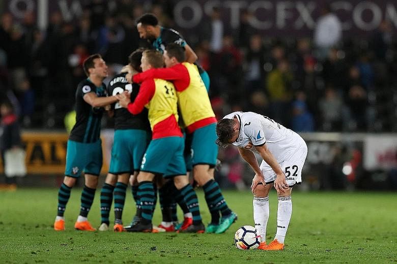 Swansea City's Connor Roberts looking dejected after the Premier League match on Tuesday as Southampton players celebrate their 1-0 win, which saw them move up to 16th place. The Swans appear likely to face the drop as West Brom became the second tea