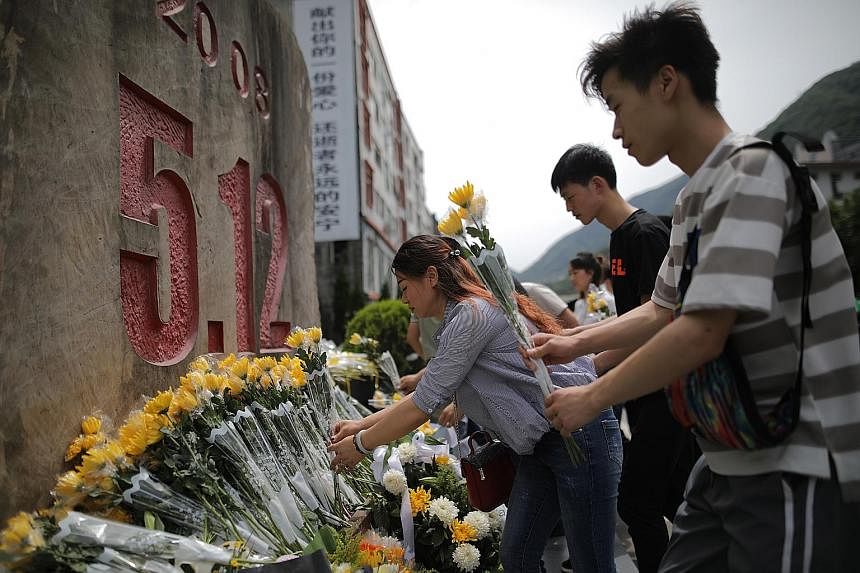 A remembrance ceremony (above) was held yesterday at a collapsed school in the town of Yingxiu, one of the worst-hit areas in the Sichuan quake. In Beichuan county (below), visitors offered flowers to mourn the victims.