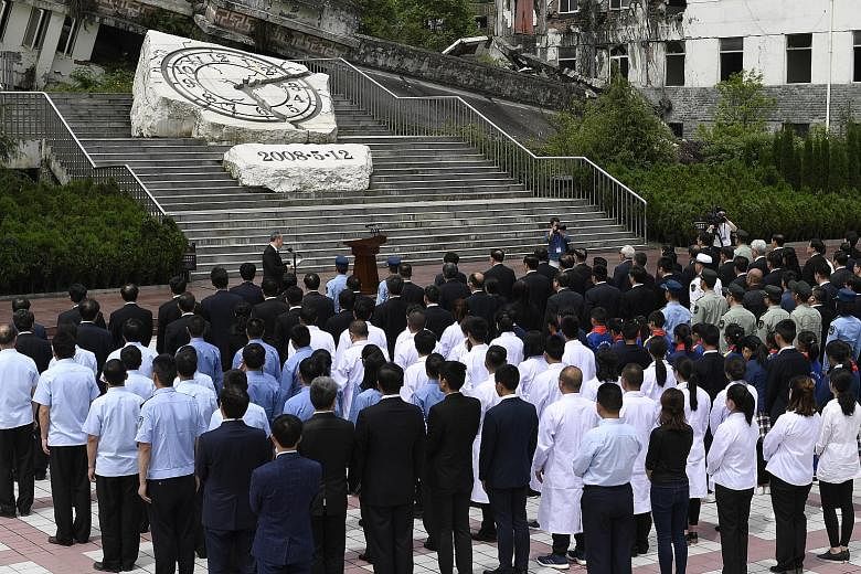 A remembrance ceremony (above) was held yesterday at a collapsed school in the town of Yingxiu, one of the worst-hit areas in the Sichuan quake. In Beichuan county (below), visitors offered flowers to mourn the victims.