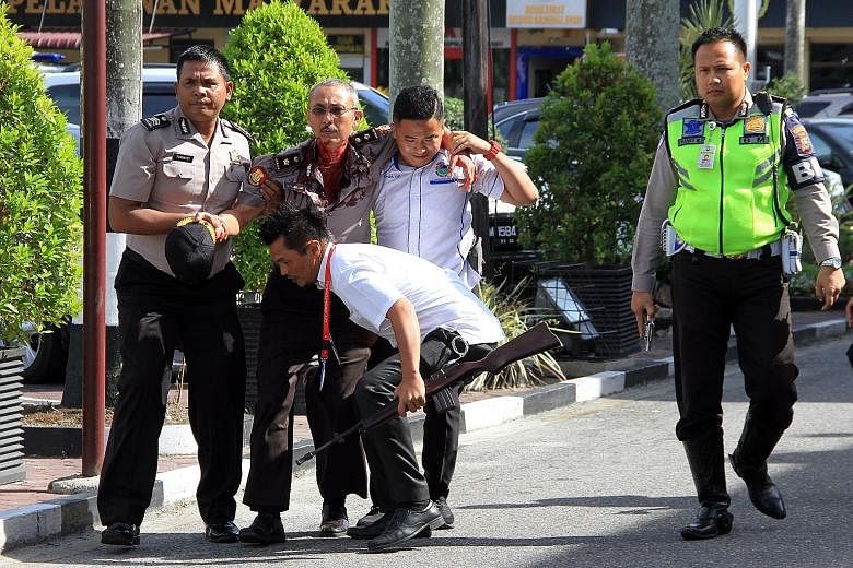 Top: An Indonesian police officer standing guard next to the body of a suspected attacker. Above: Indonesian police officers helping an injured colleague following the attack at the Pekanbaru police station by men using samurai swords. An Indonesian 