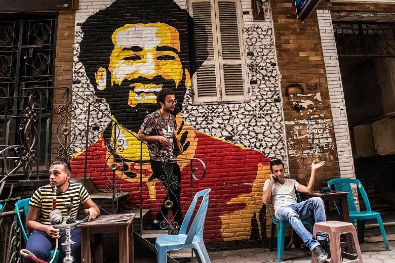 Ahmed Fathy, a 26-year-old Egyptian artist, on the stairs at an open-air cafe in Cairo. He painted the mural depicting the smiling face of Liverpool forward Mohamed Salah.