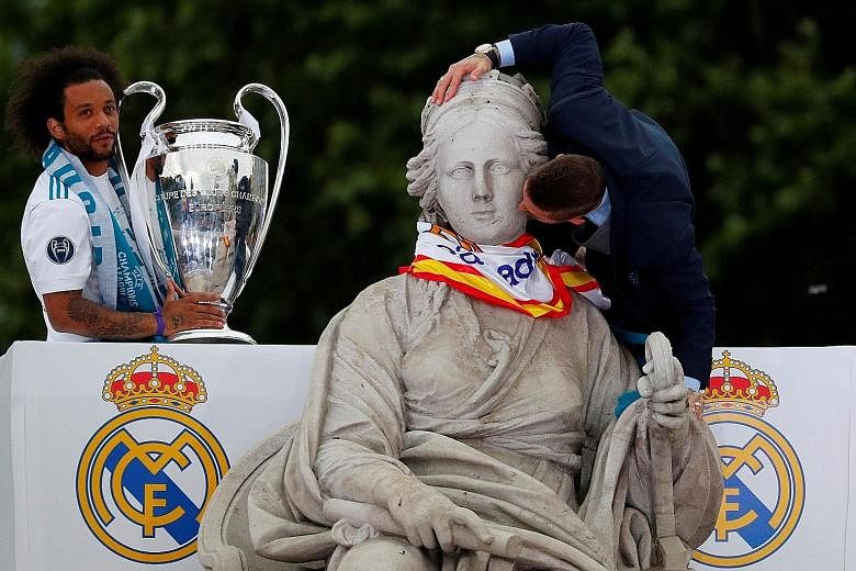 Real Madrid captain Sergio Ramos giving the Greek goddess Cybele, the ancient Phrygian Mother of the Gods, a peck on her cheek while team-mate Marcelo keeps watch over the Champions League trophy during the team's victory parade past the iconic Plaza