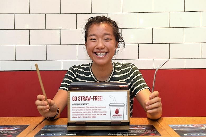 Student Ang Zyn Yee with a wooden straw and a metal straw which she carries with her at all times, and the sticker that she designed for fast-food chain 4Fingers Crispy Chicken, which encourages diners to go straw-free.