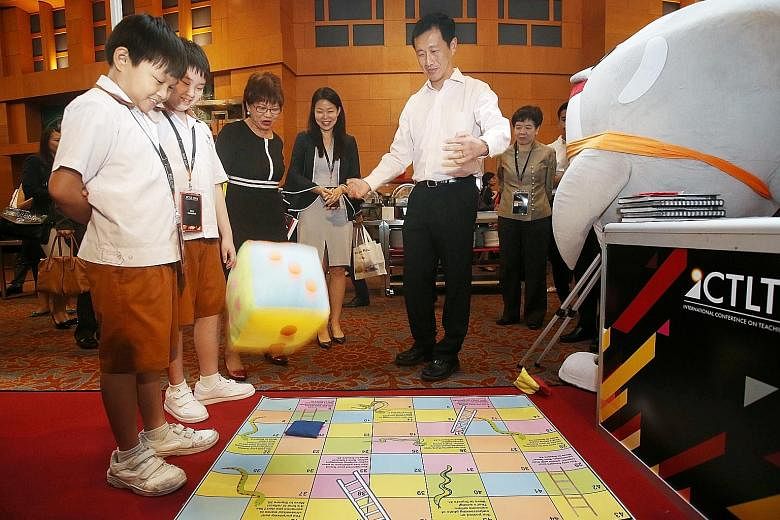 Education Minister Ong Ye Kung throwing a dice as he played a game of snakes and ladders focused on the theme of cyber wellness, created by Ahmad Ibrahim Primary School pupils Austin Kho (left) and Loo You En (second from left), and their teachers. W