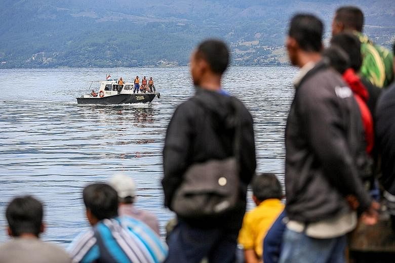 Residents waiting as members of an Indonesian search and rescue team look for victims from the sunken boat in Lake Toba, Sumatra, yesterday. Besides divers and underwater vehicles, about 400 personnel have been deployed to search the huge lake in an 