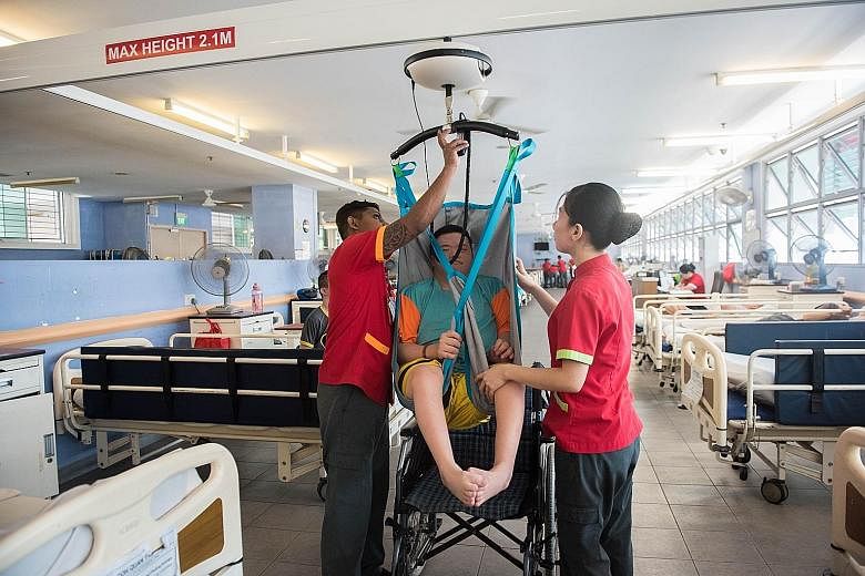 Healthcare aide Nalawayaa Suranga (left) and nursing aide Glaiza Minasalvas hoisting up Mr Goh Quan Yao at the Red Cross Home for the Disabled to transfer him from the bed to the wheelchair. The aides no longer need to strain to lift bed-bound patien