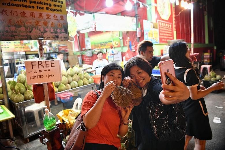 Above: Sam Fruit Trading in Tampines, which had given out free durians on Monday, was swamped by customers. Left: Friends Alice Leung and Gracia Tan with their free durians in Balestier Road.