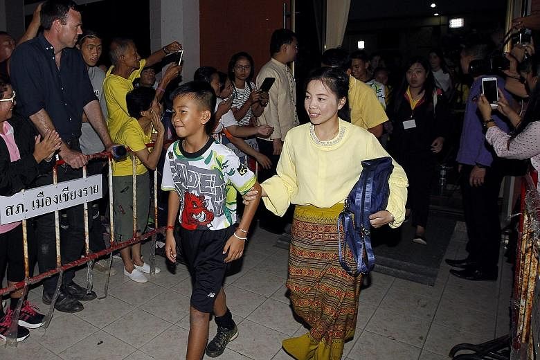 One of the members of the Wild Boars football team being accompanied by his mother as they walk past well-wishers after a media conference in Chiang Rai, Thailand, yesterday. The boys were all dressed in black shorts and T-shirts emblazoned with a re