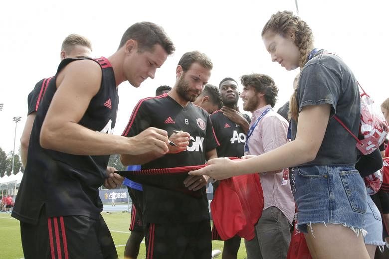 Manchester United players, including Juan Mata (centre), sign autographs for fans before practice at Drake Field at UCLA in Los Angeles. United, depleted by World Cup absentees, face Italian side AC Milan in an International Champions Cup match at th