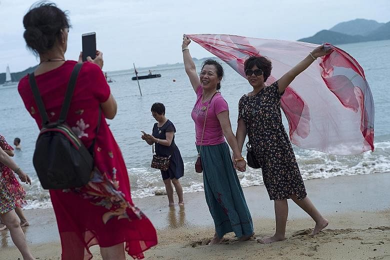Mainland Chinese tourists on a beach in Hong Kong. Beijing's move to support China's slowing economy has led to a weaker Chinese currency. This, coupled with a strong Hong Kong dollar, could translate into fewer mainland tourists visiting the territo