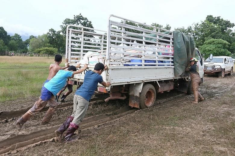 Volunteers pushing a lorry carrying supplies from the Singapore Red Cross (SRC), after it got stuck in thick mud at the Sanamxai Secondary evacuation centre yesterday. The SRC advance team will distribute items to evacuees today. Children enjoying af