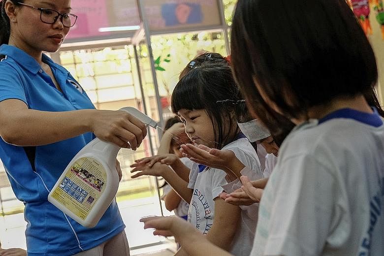 A teacher at a pre-school in Setapak, Kuala Lumpur, spraying sanitiser on children's hands (above) as a precaution against hand, foot and mouth disease, and checking a child's mouth (below) for symptoms of the disease last week. Most Malaysian states