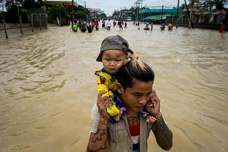 A baby being carried through flood waters in the Bago region, Myanmar, yesterday. Heavy monsoon rains have pounded the region in recent days and show no sign of abating.