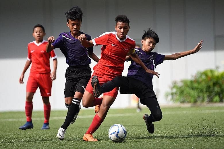 Singapore Sports School captain Amir Syafiz Abdul Rashid (centre, in red) challenged by two Queensway Secondary School players during the Schools National C Division football final at Our Tampines Hub yesterday. Amir scored the winning goal in SSP's 
