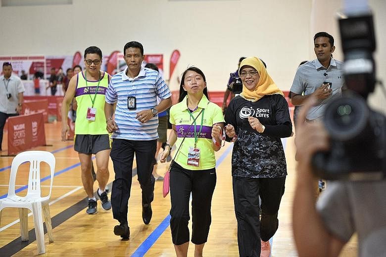 President Halimah Yacob taking on the guide's role for visually impaired runner Patricia Poo during the Inclusive Sports Festival at the Singapore Sports Hub yesterday. The festival offers the public a chance to experience how para-athletes compete i